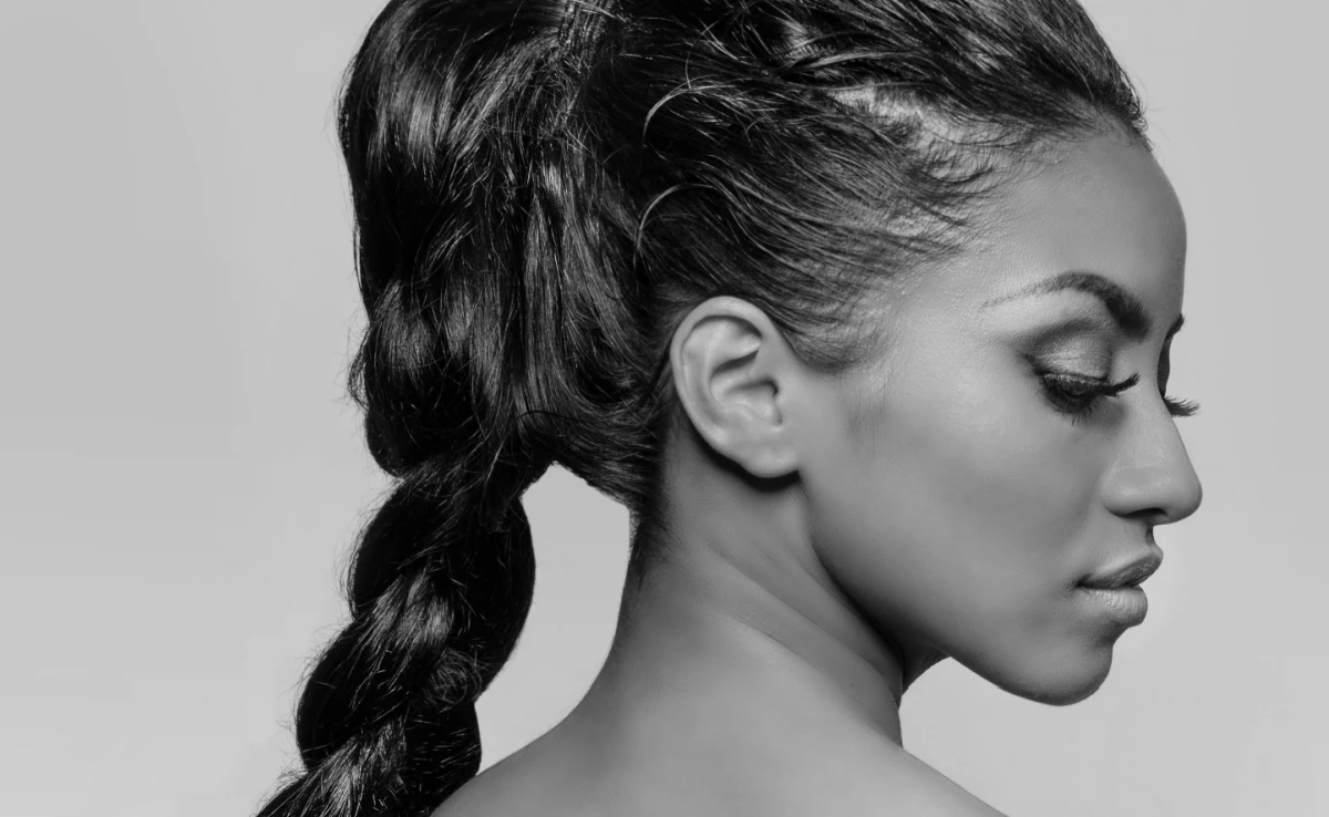 Beautiful woman's face in profile, hair braided; isolated against light grey background.