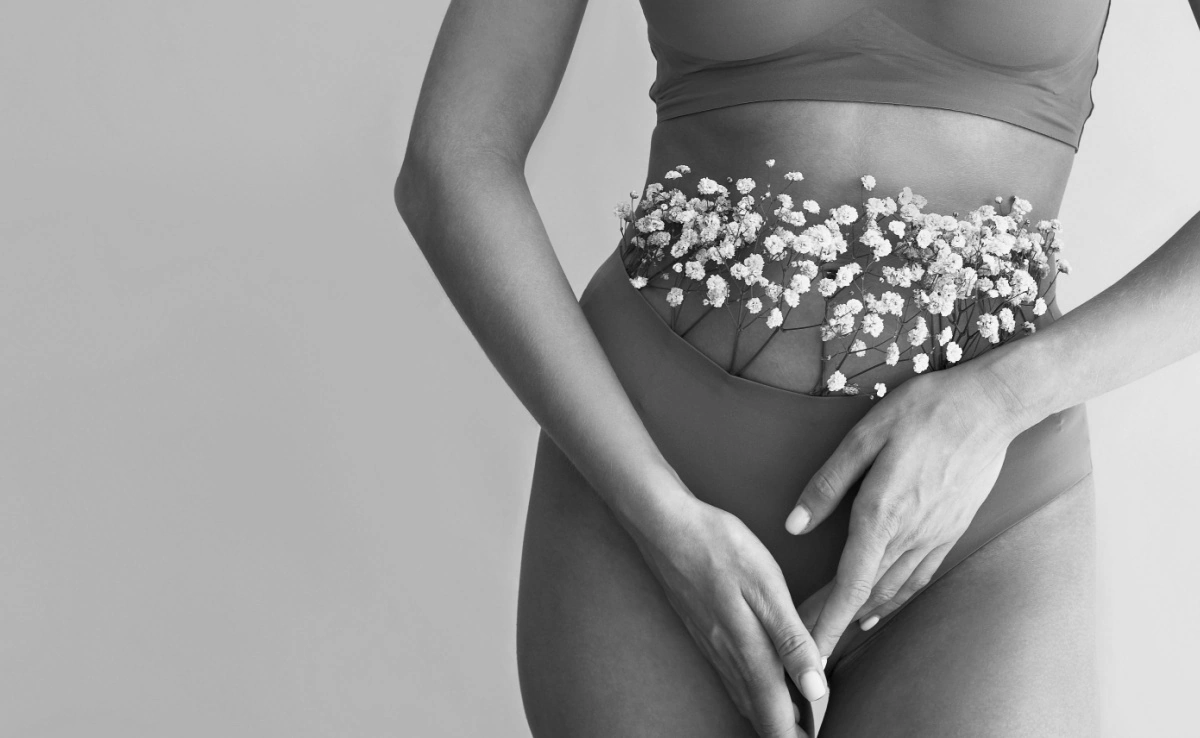 Cropped image of woman posing in lingerie with flowers on beige background.