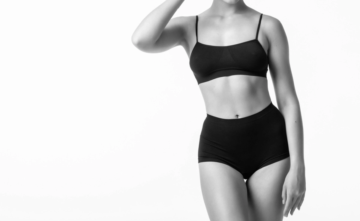 Laughing sporty girl in black bikini posing on grey background.