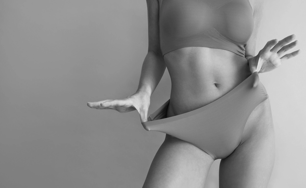 Cropped image of beautiful tanned young woman posing in comfortable underwear on beige background.
